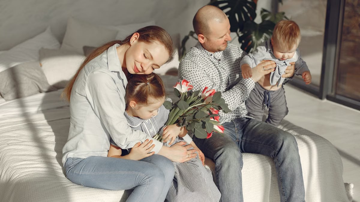 Cheerful parents with children wearing casual clothes smiling while playing with daughter and son in bedroom together during weekend at home